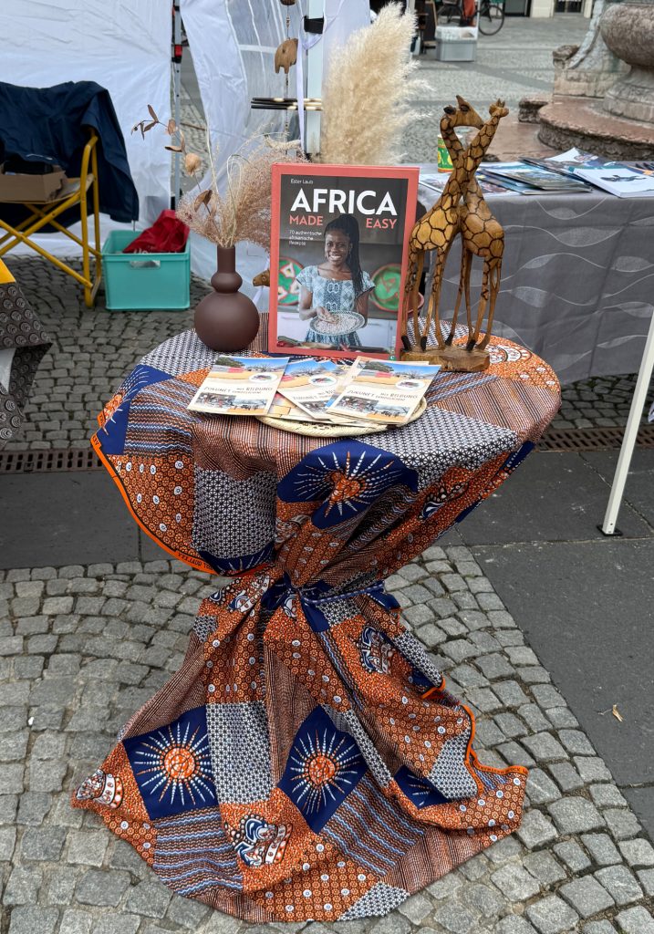 Der liebevoll gestaltete Informationsstand von Kwafa Namibia e.V. beim Fest der Vielfalt 2026 in Bamberg mit Roll-up, Informationsmaterialien, namibischer Dekoration,  traditionellen Handwerksstücken und Africa Made Easy Kochbuch..